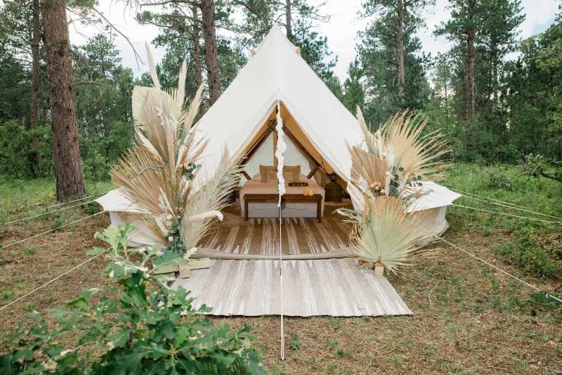 A white tent with rugs and a table sits in the forest decorated with pampa grass.