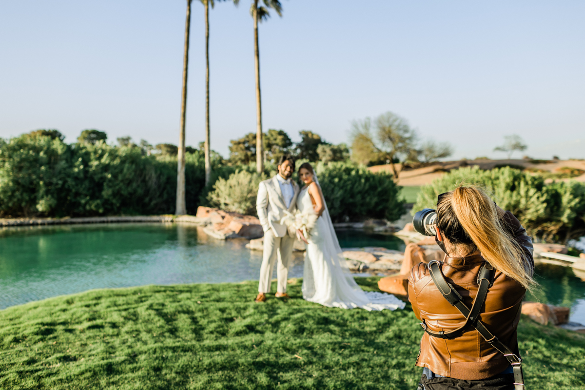 Wedding photographer taking photographs of a bride in groom in the background.