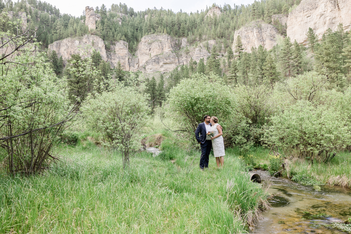 Groom kissing his bride near a creek in a canyon.