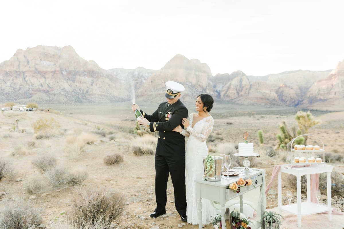 Groom popping top off of a champagne bottle while celebrating a wedding with his bride.