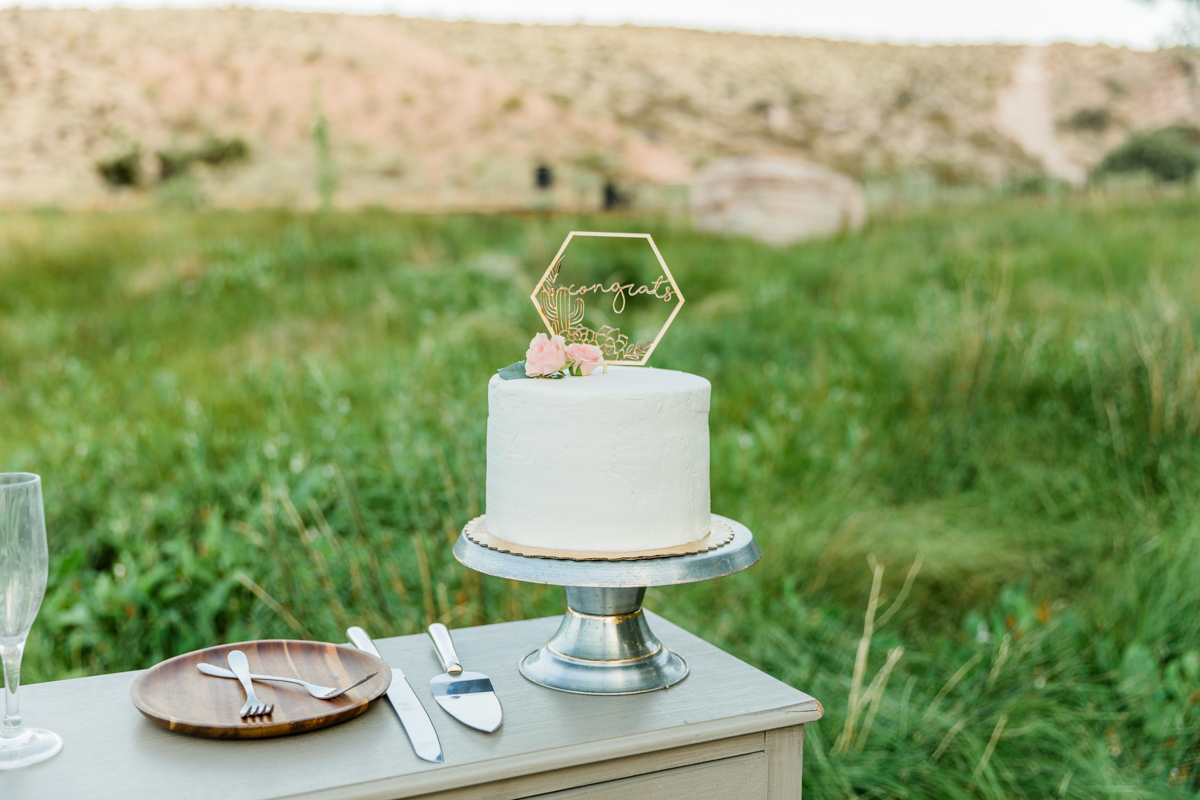 Small, white wedding cake sitting atop a small table next to plate and utensils.