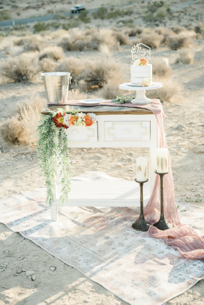 Wedding ceremony celebration table with flowers, candles cake and a champagne bucket arranged in a bushy desert landscape.