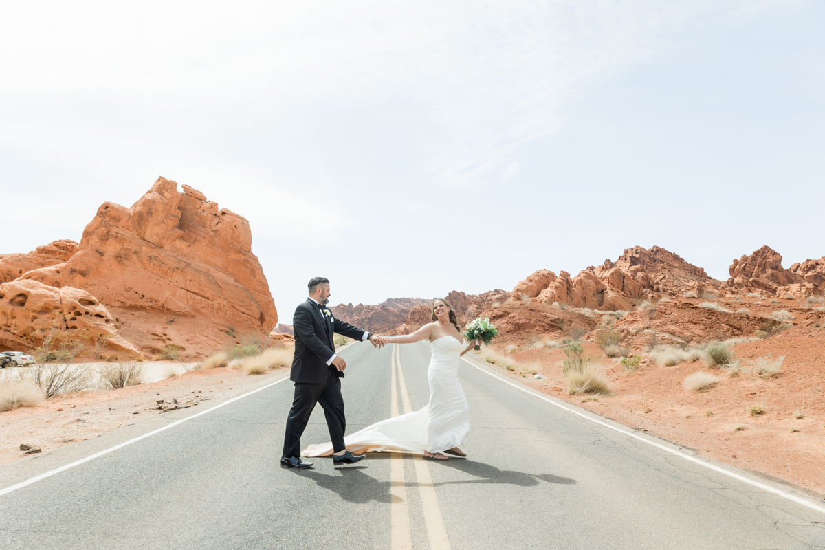 Bride and groom in the desert holding hands while crossing the road.