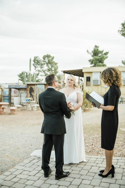 A bride and groom stand before a wedding officiant performing a marriage ceremony on a small brick patio. A bride and groom stand before a wedding officiant performing a marriage ceremony on a small brick patio.