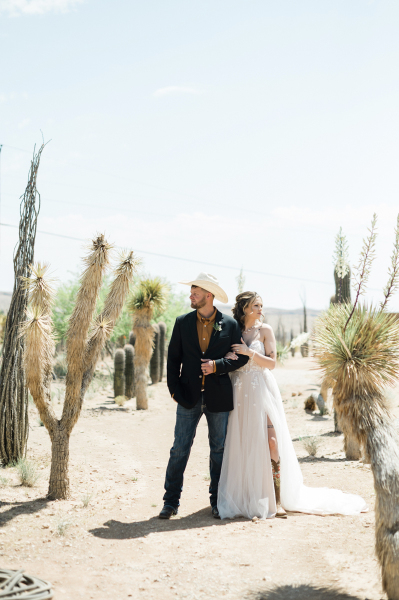 A groom and bride hold each other and look opposite ways as they stand between rows of Joshua Trees. A groom and bride hold each other and look opposite ways as they stand between rows of Joshua Trees.