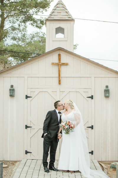 A groom and bride kiss while standing in front of the doors of a little wooden chapel. A groom and bride kiss while standing in front of the doors of a little wooden chapel.