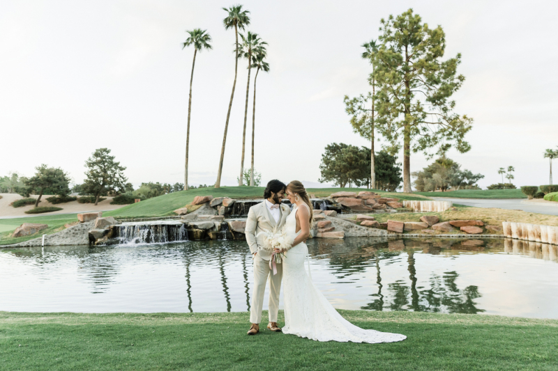 Newly wed couple standing, touching foreheads, in front of golf course water area.
