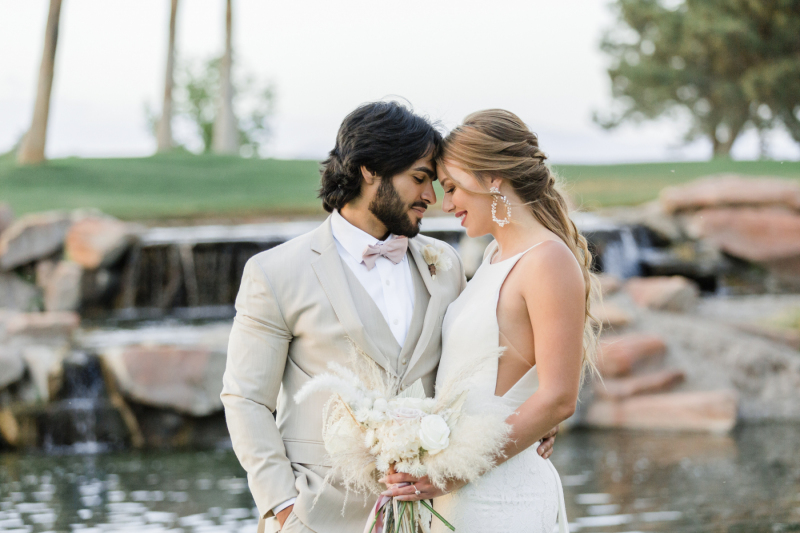 Newly wed couple standing, touching foreheads, in front of golf course water area.