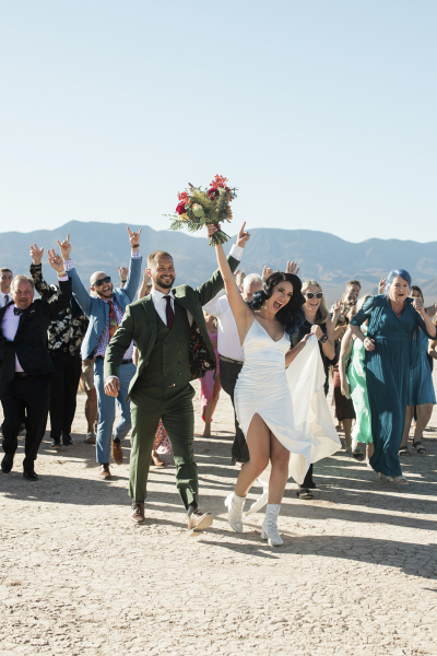 A bride and groom and their wedding party all walk towards the camera. The entire group is raising their arms, pumping their fists and hooting and hollering with joy. They are on the Dry Lake Bed near Las Vegas. A bride and groom and their wedding party all walk towards the camera. The entire group is raising their arms, pumping their fists and hooting and hollering with joy. They are on the Dry Lake Bed near Las Vegas.