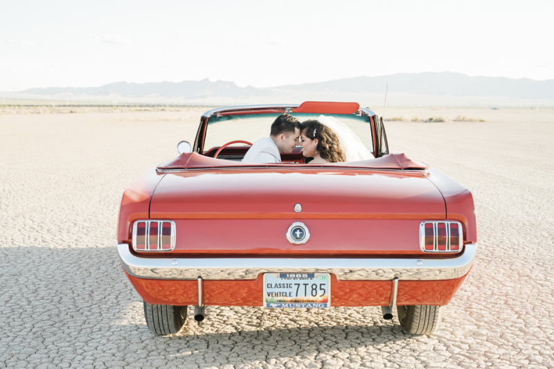 A man and woman sit in the front seats of a 1965 Ford Mustang convertible. The photo is taken from behind the car. The top is down. They are posing for wedding photos on the Dry Lake Bed south of Las Vegas, Nevada. A man and woman sit in the front seats of a 1965 Ford Mustang convertible. The photo is taken from behind the car. The top is down. They are posing for wedding photos on the Dry Lake Bed south of Las Vegas, Nevada.