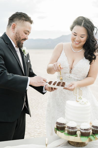 A groom and bride use golden forks to dig into a piece of chocolate wedding cake. The cake is being served at their wedding on the Dry Lake Bed near Las Vegas. A groom and bride use golden forks to dig into a piece of chocolate wedding cake. The cake is being served at their wedding on the Dry Lake Bed near Las Vegas.