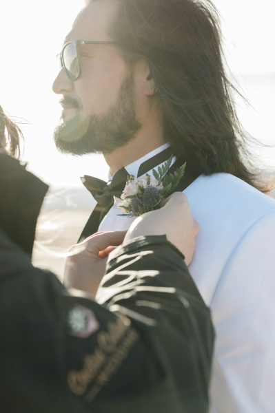 A boutonniere is pinned onto a groom's lapel. He is wearing a white tuxedo jacket and a black bowtie.He sports a beard, long hair and sunglasses. A boutonniere is pinned onto a groom's lapel. He is wearing a white tuxedo jacket and a black bowtie.He sports a beard, long hair and sunglasses.