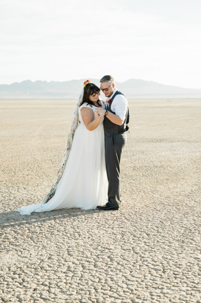 A bride and groom slow dance together on their wedding day. It is a sunny afternoon and they are wearing sunglasses. Their dance floor is the dry and cracked ground of the Dry Lake Bed outside of Las Vegas. A bride and groom slow dance together on their wedding day. It is a sunny afternoon and they are wearing sunglasses. Their dance floor is the dry and cracked ground of the Dry Lake Bed outside of Las Vegas.