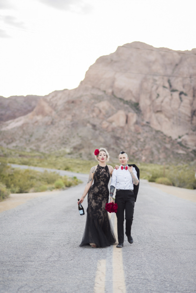 A woman in a long lacy black dress and a woman sporting a mohawk haircut walk down the middle of the road which winds through Eldorado Canyon.