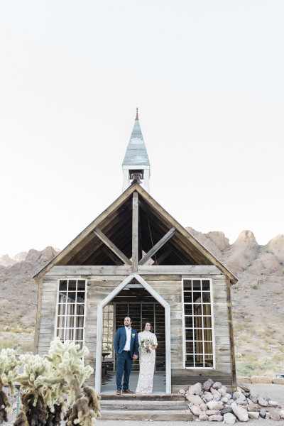 Wide shot of a groom and bride standing in the doorway of the rustic wooden chapel in Eldorado Canyon.