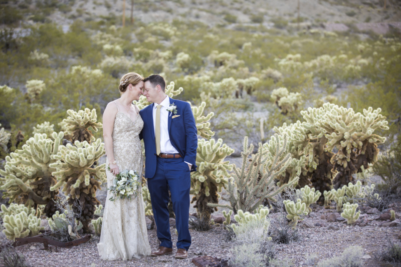 A bride and groom rest their foreheads against each other as they pose for photos in a cholla cactus field.