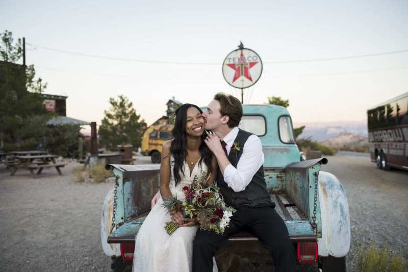 A bride is kissed by her groom as they sit on the tailgate of a vintage truck in Eldorado Canyon near Las Vegas.