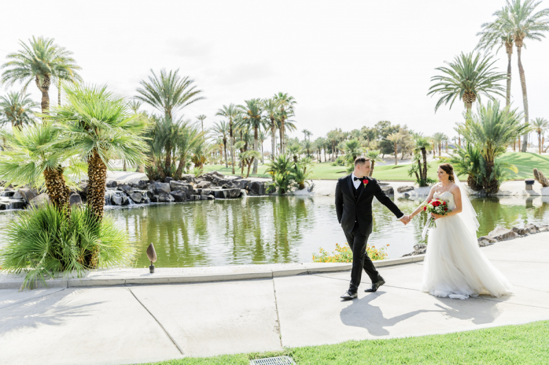 Bride and groom walking along golf path in front of pond.
