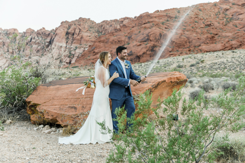 Newlywed couple opening champagne bottle.