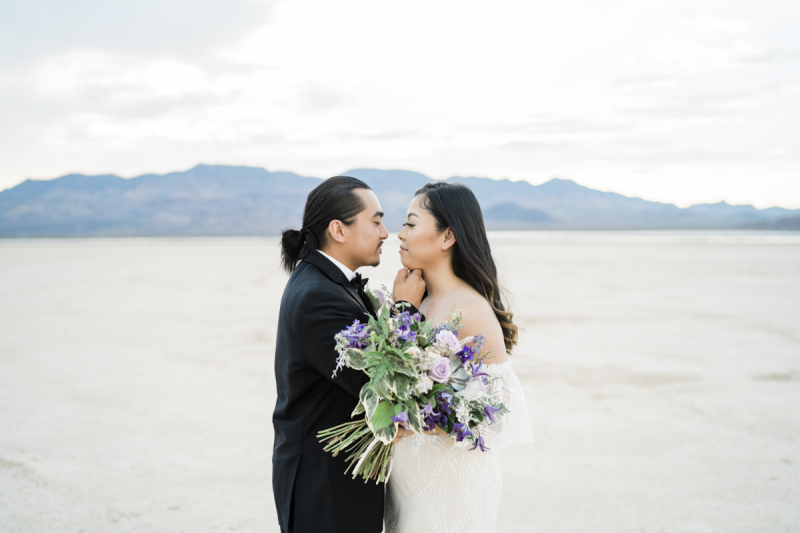 Newlywed couple standing face to face with desert background.