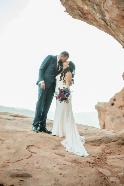 Groom kissing bride on mountain rock.