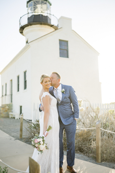 Groom kisses bride in front of lighthouse.