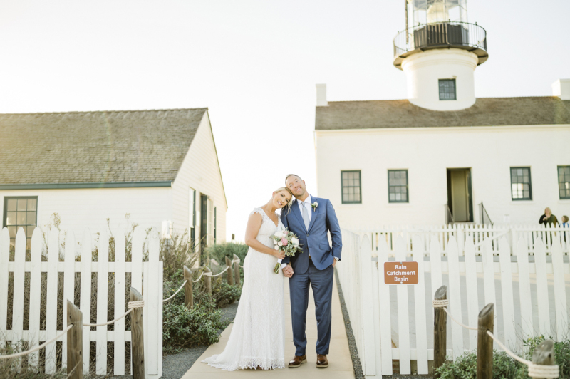 Couple standing arms around each other by a white picket fence.
