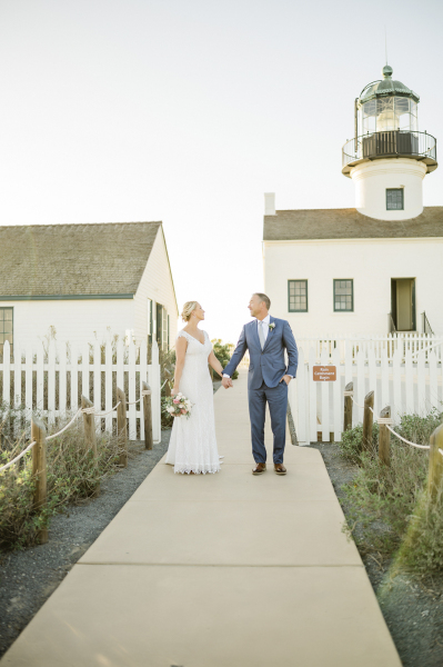 Bride and groom holding hands by white picket fence.