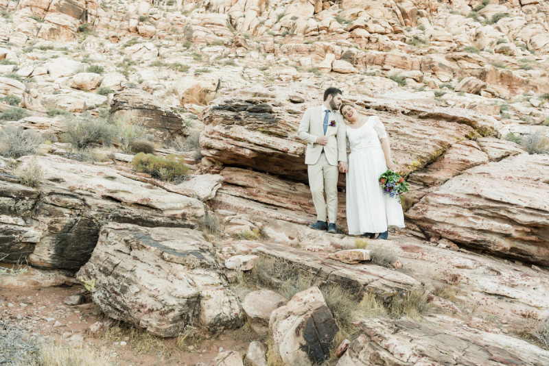 Bride and groom standing on mountainous rocks.
