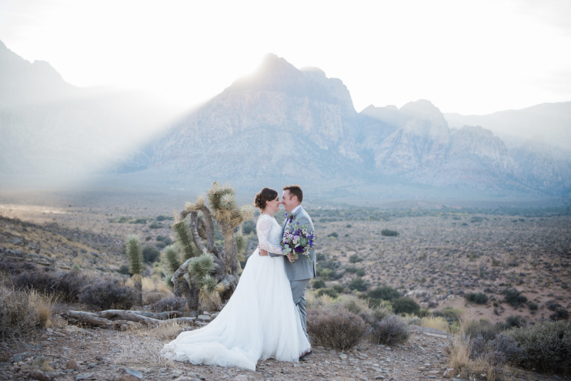 Newlywed couple looking into each other's eyes while sun sets behind mountain.