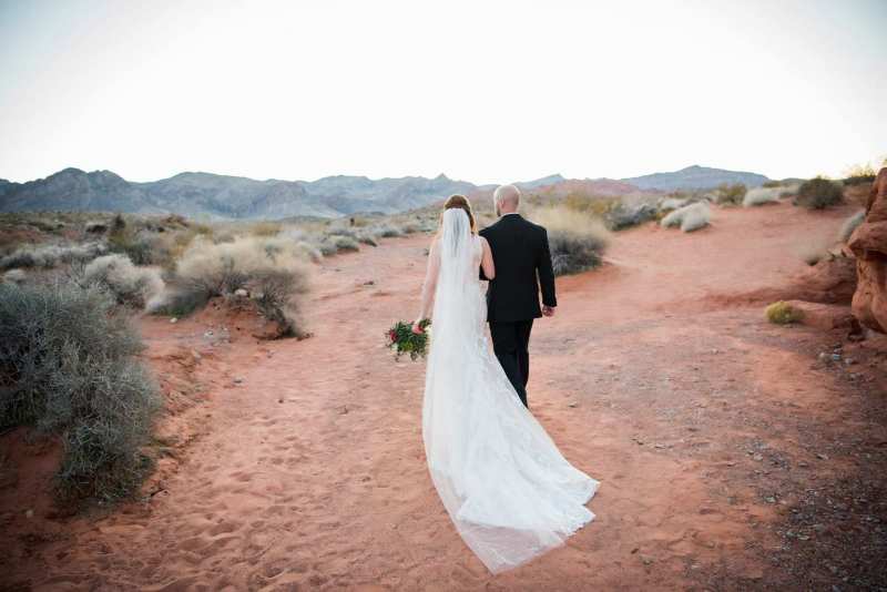 Bride and groom walking away through desert trail.