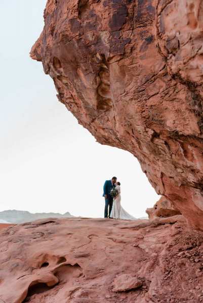 Bride and groom standing under mountain with landscape background.