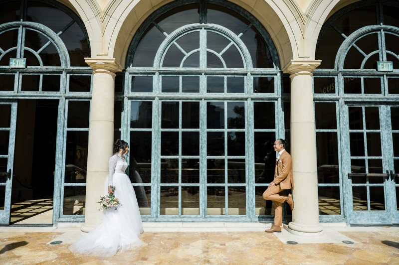 Bride and groom standing in front of ceiling high windows.
