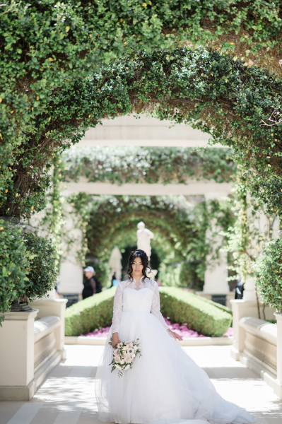 Bride standing in archway of green leaves.