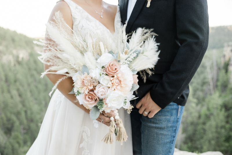 A tightly cropped photo of a bride standing next to a groom with only their torsos visible as the woman holds her bouquet of flowers for the camera.