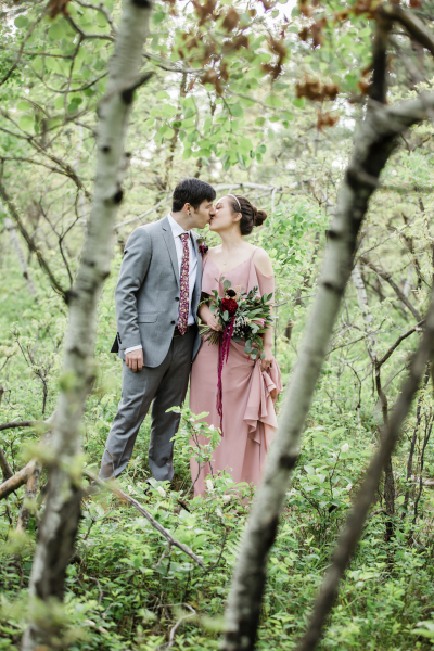 A blurry pair of aspen tree trunks frame a couple kissing in the woods on their wedding day in the Black Hills of South Dakota.