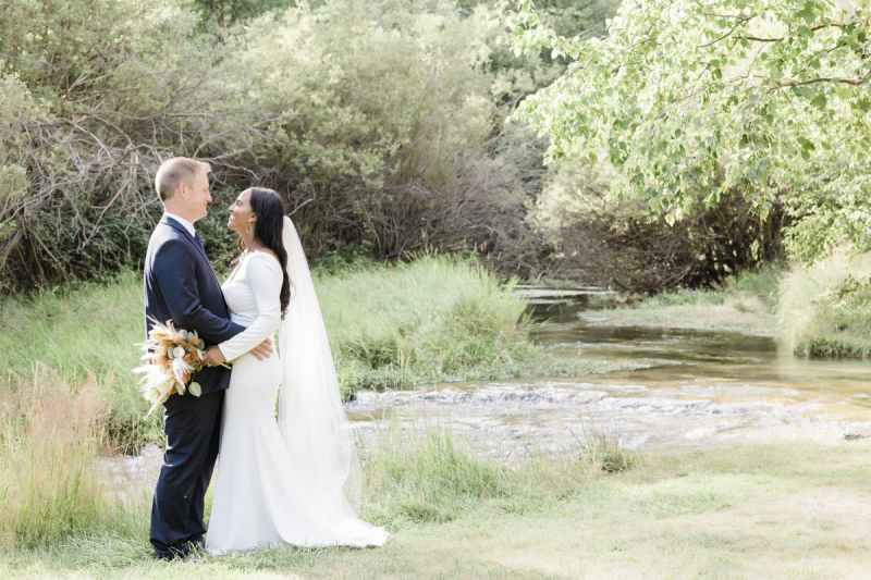 A newly married couple stands near the edge of a stream in the woods. They are posing for wedding photos in the Black Hills of South Dakota.