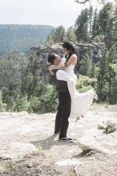 A groom lifts his bride off the ground and holds her against his chest as the two look lovingly at each other on their wedding day in the Black Hills of South Dakota.