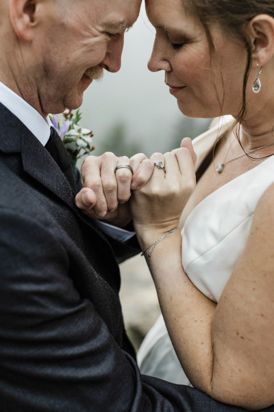 A close-up image of a mature couple touching foreheads and locking pinky fingers as they embrace closely on their wedding day in South Dakota\'s Black Hills region.