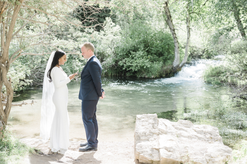 A bride and groom stand at the edge of a gently sloping creek bank as she reads her vows to him. They are holding their wedding in the Black Hills of South Dakota.