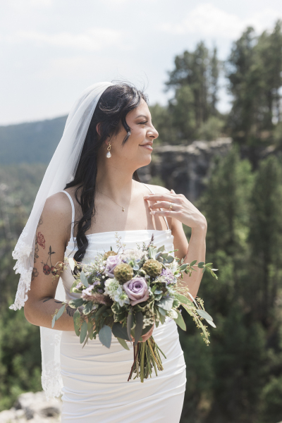 A bride with a sleeveless wedding dress that shows off her tattoos poses for a portrait on her wedding day in the Black Hills of South Dakota.