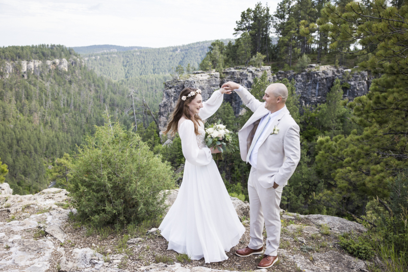 A bride and groom act like they are dancing near the edge of a cliff in the Black Hills of South Dakota. The groom twirls the bride.