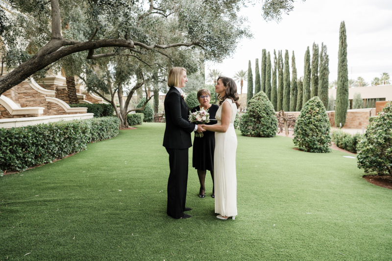 Two women hold hands and smile at each other as they are married by an officiant in a garden at Green Valley Ranch. Two women hold hands and smile at each other as they are married by an officiant in a garden at Green Valley Ranch.