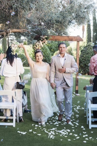 A bride and groom walk hand-in-hand down the aisle at the conclusion of their wedding ceremony. She lifts her flowers skyward.