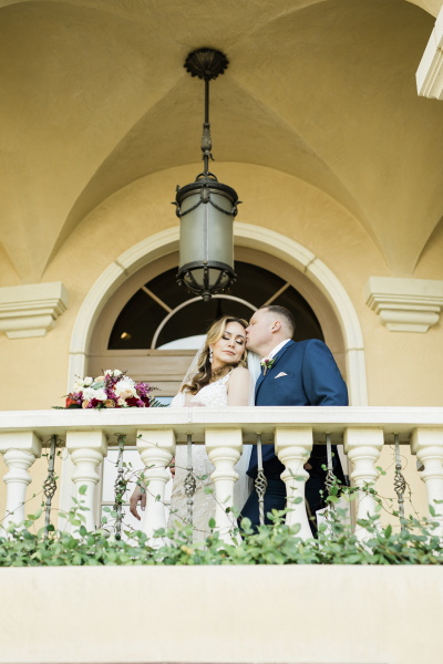 Looking upwards at a bride and groom on a balcony as the groom kisses the bride.