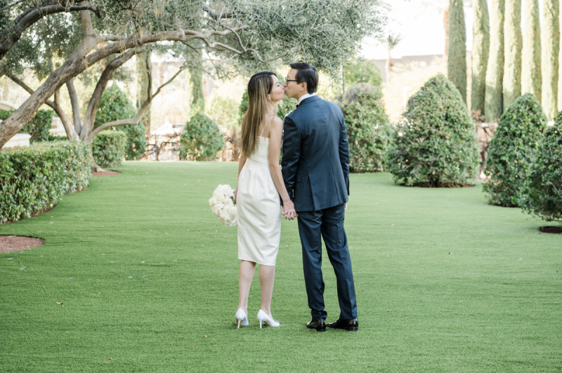 A bride and groom with their backs to the camera turning towards each other and kissing in a garden.