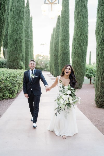 Groom and bride holding hands, with joyful faces.