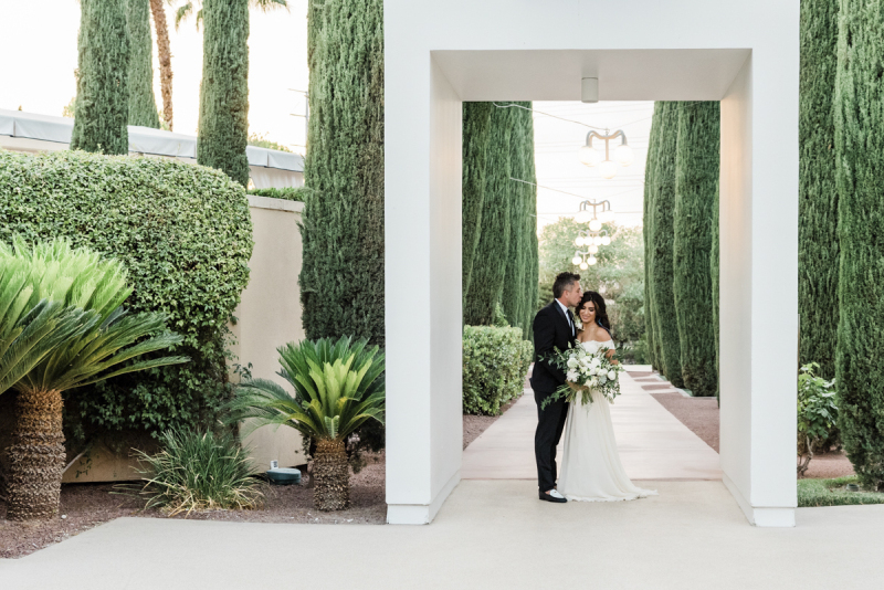 Bride and groom in rectangular archway on paved hotel path.
