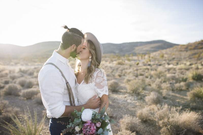 Bride and groom kissing with desert landscape in the background.