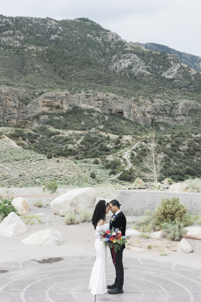 A bride and groom bow their foreheads to touch each other as they stand in the center of a paved spiral design built into the ground.